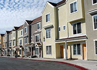 A street lined with three-story stucco townhome-style units in earth-tone colors.